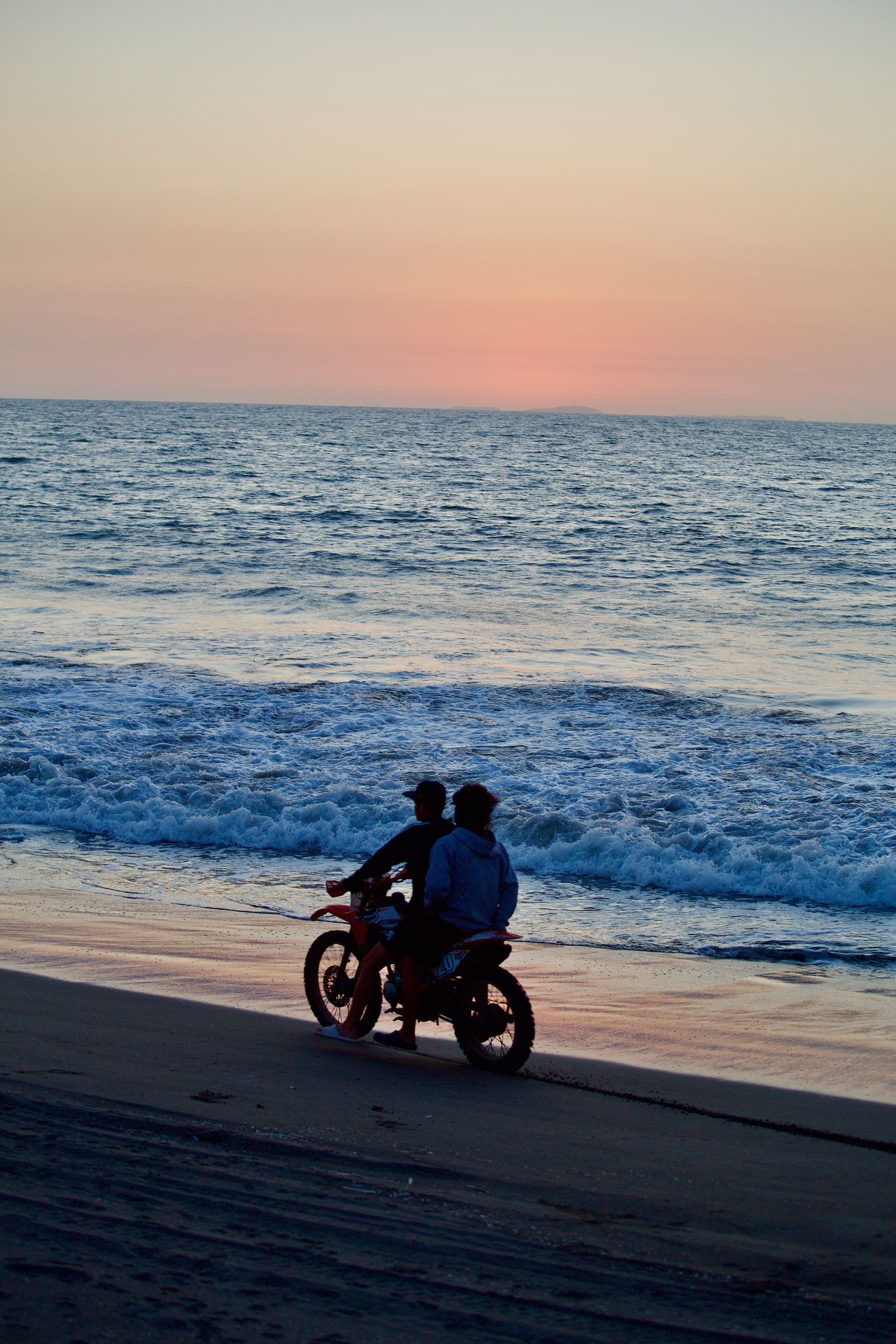 Dva motorkáři na pláži při západu slunce